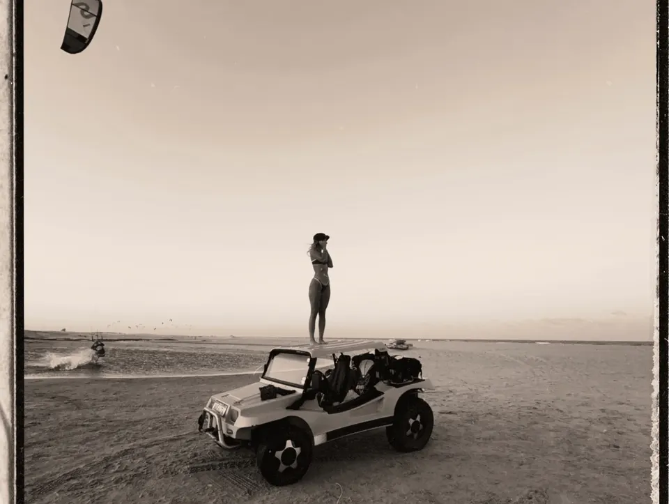 Standing on a beach buggy at the water's edge, kites in the sky over the lagoon in Taiba, Brazil